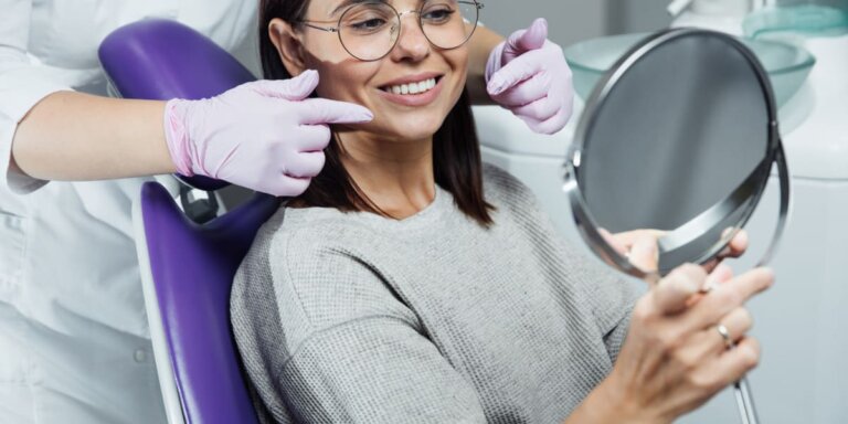 Mujer con gafas mirando su sonrisa en un espejo desde el sillón dental