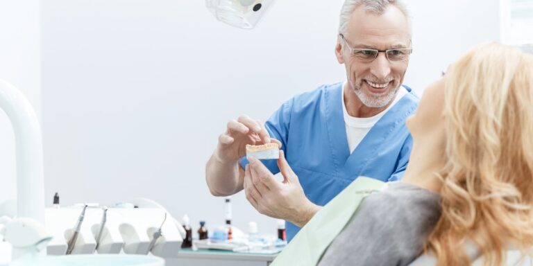 Buen dentista: el dentista enseña a una paciente un modelo de dientes de escayola y le explica el tratamiento