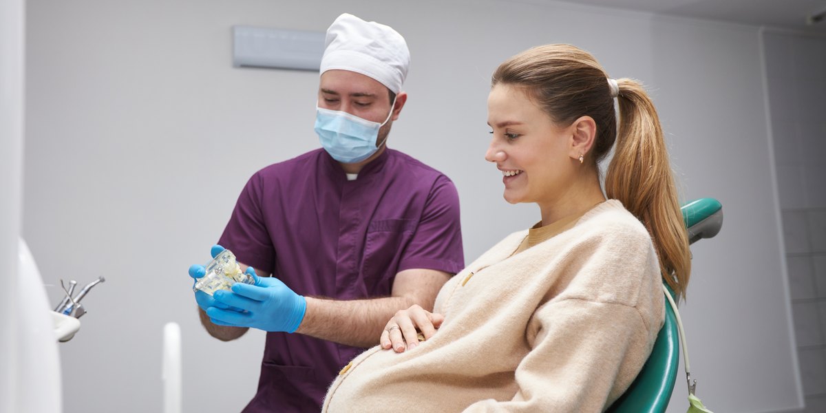 Dentista en el embarazo: mujer embarazada en el sillón dental mientras el dentista le explica la revisión con un modelo de la boca