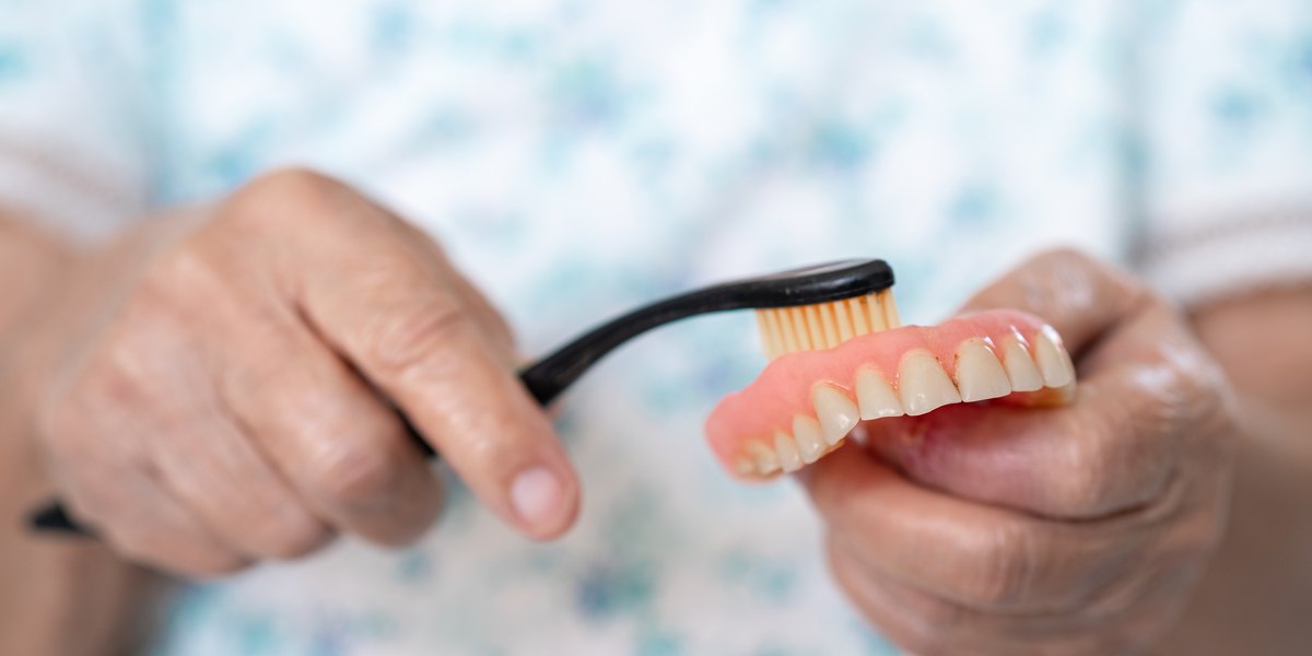 Pegamento para dentaduras postizas: unas manos limpian con un cepillo una dentadura postiza superior