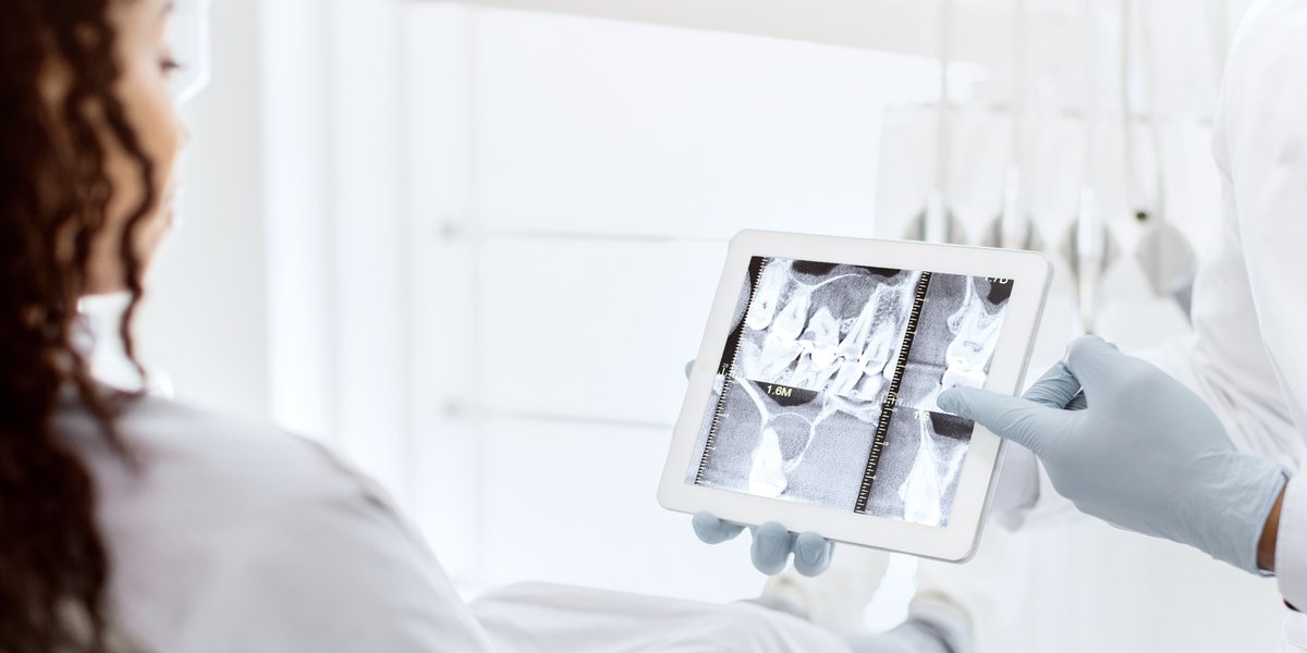 Flemón: el dentista muestra a una paciente la radiografía de sus muelas en una tableta