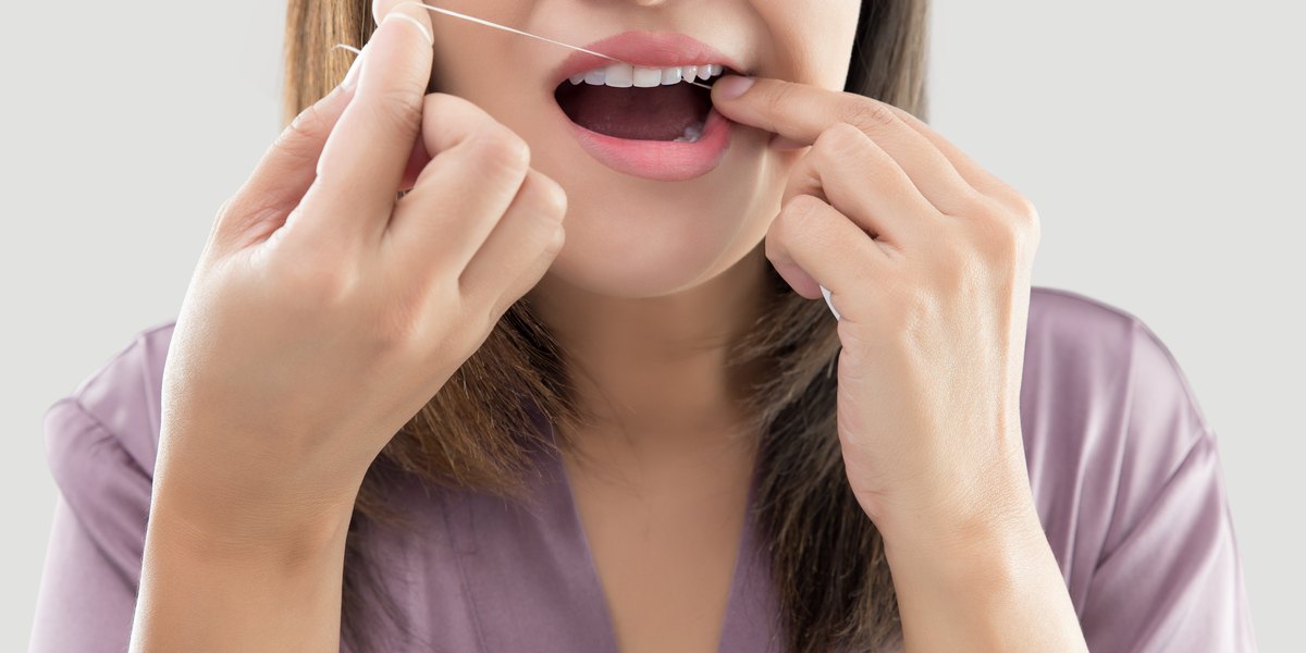 Mujer limpiando los dientes con hilo dental