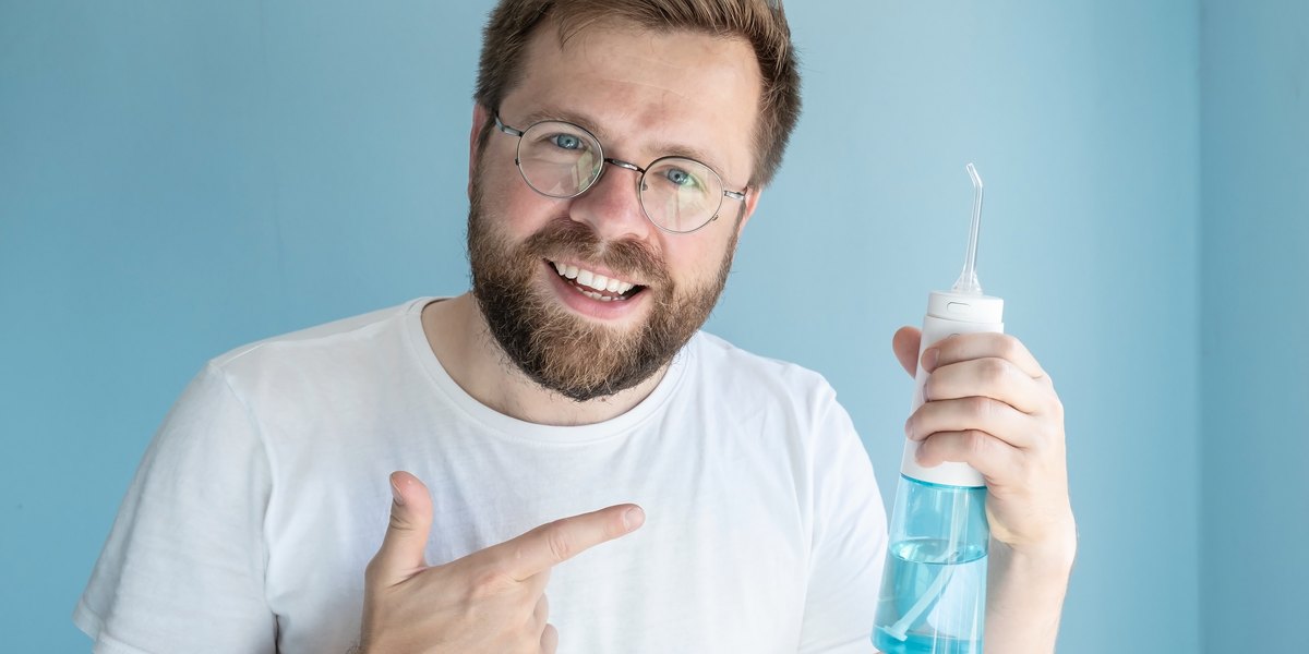 Irrigador dental: un hombre sostiene un irrigador portátil y lo señala con el dedo