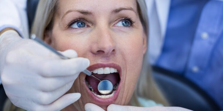Odontólogo: el dentista explora con un espejo dental la boca abierta de una paciente