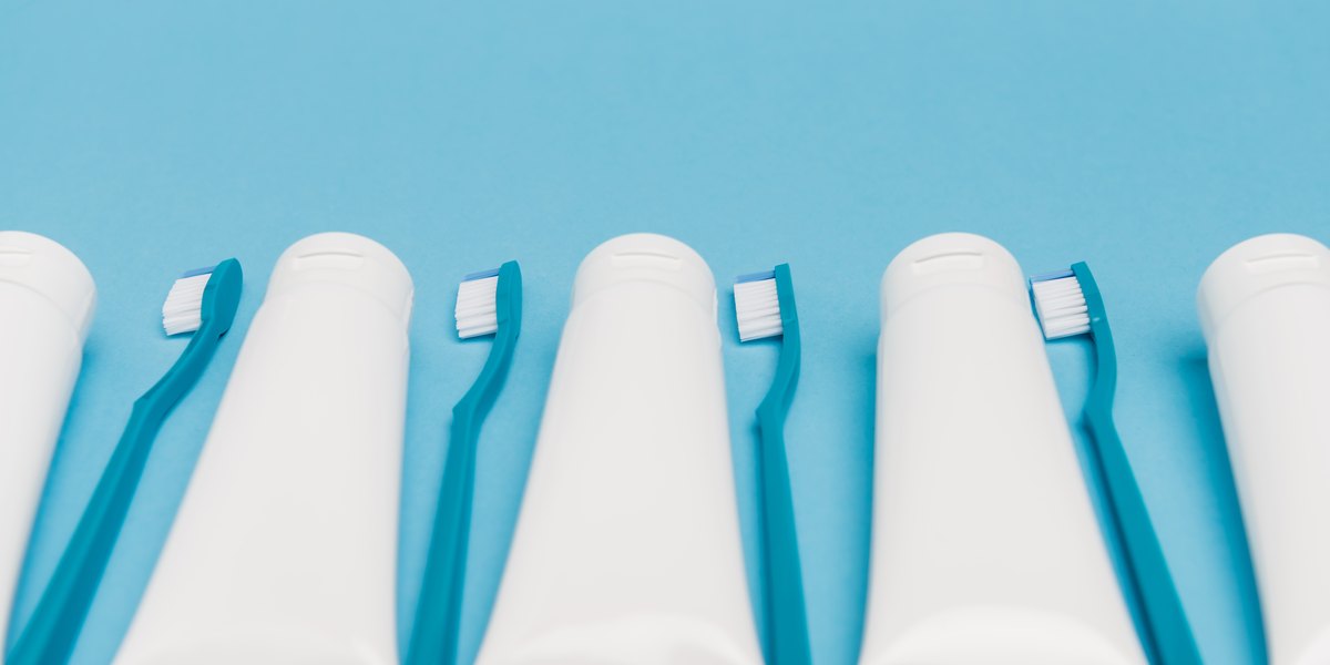 Pasta de dientes: tubos blancos sin marca alternados con cepillos de dientes turquesa sobre un fondo azul claro