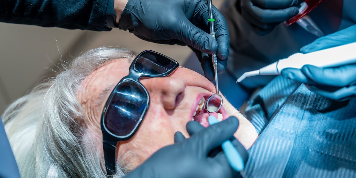 Piorrea: dos dentistas revisan las encías de una paciente mayor con sonda y espejo