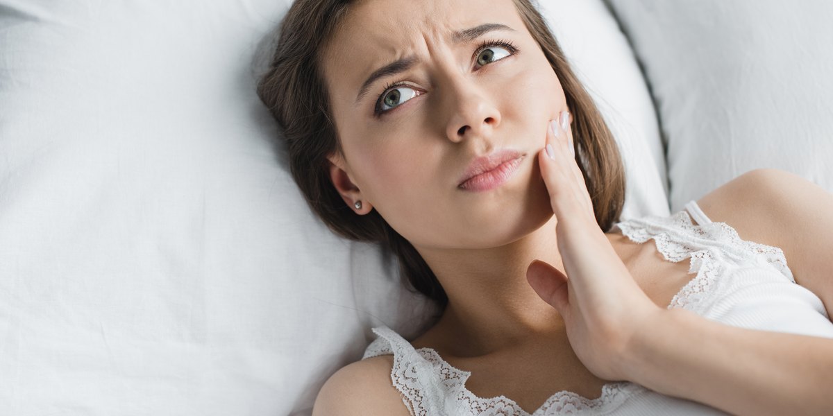 Postoperatorio de un implante dental: una mujer descansa tumbada en la cama con la mano en la mandíbula por la molestia