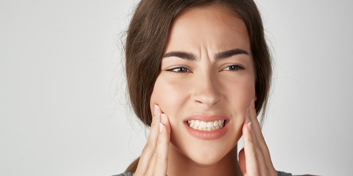 Sensibilidad dental: una mujer con gesto de dolor se sujeta las mejillas y aprieta los dientes