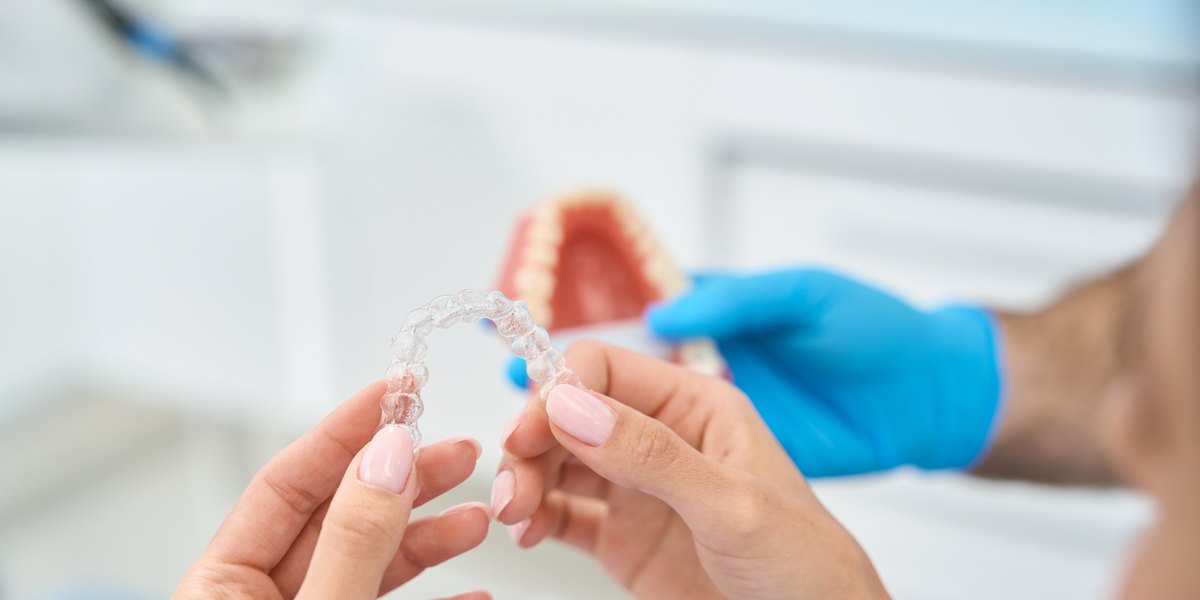 Stripping dental: una paciente sostiene su alineador transparente mientras el dentista le enseña un modelo de dientes