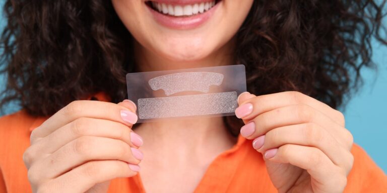 Mujer joven que sostiene tiras blanqueadoras de dientes sobre fondo azul claro, primer plano